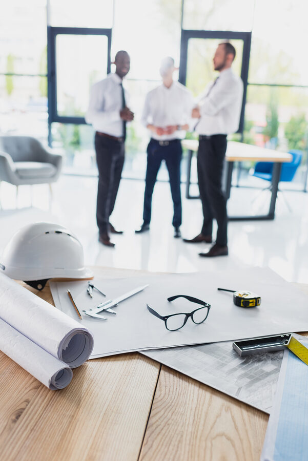 various architecture supplies on workplace with architects behind, focus on foreground
